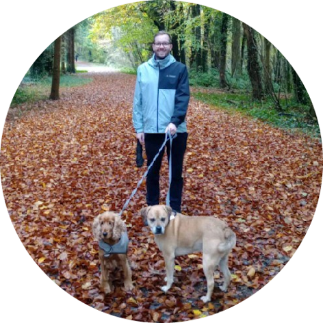 An autumnal photo of Michael with his two dogs on a walk in a forest.