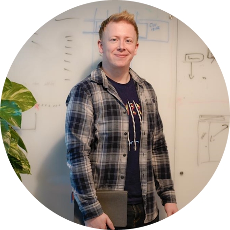 Mick standing in front of a whiteboard holding a notebook.